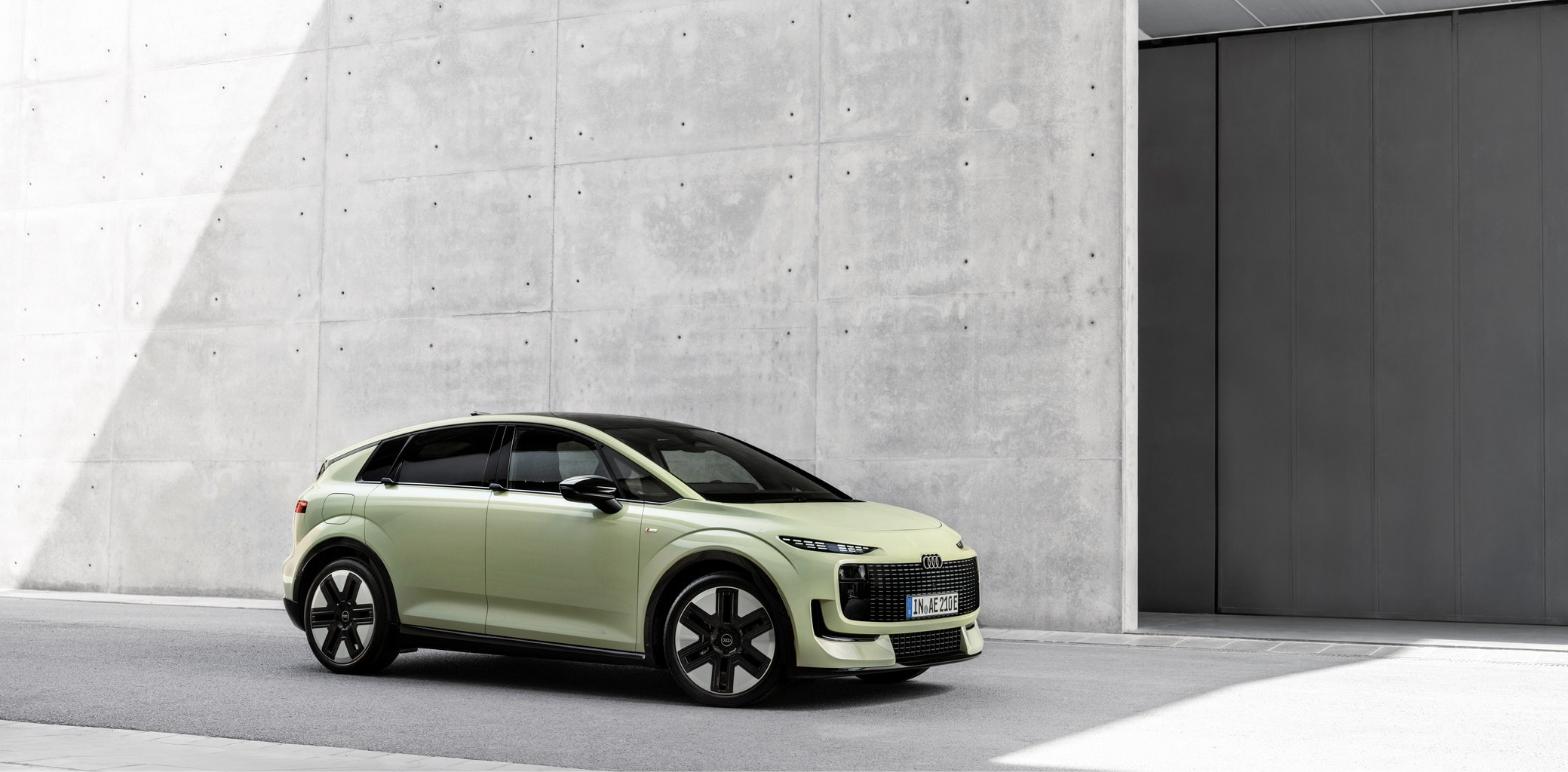 Audi A2 e-tron açık yeşil gövdesiyle beton bir binanın önünde