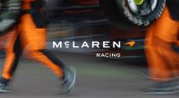 Pit alanında McLaren Racing yazısı ve turuncu tulumlu ekip
