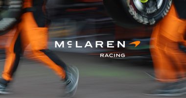 Pit alanında McLaren Racing yazısı ve turuncu tulumlu ekip