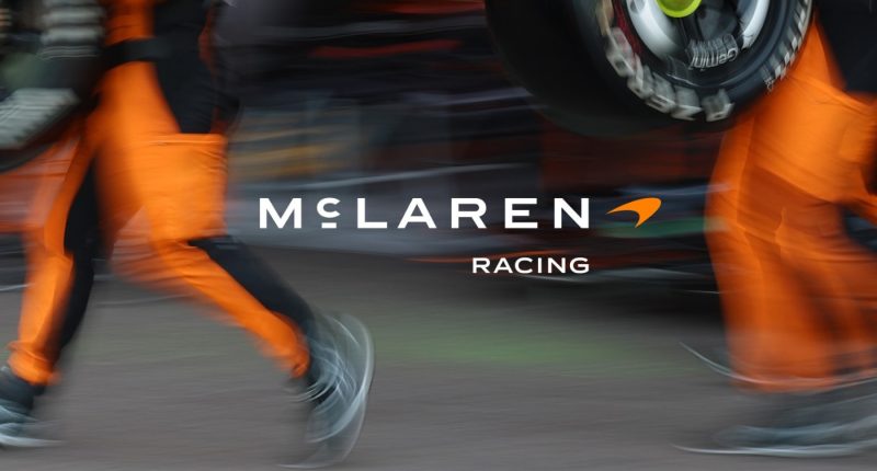 Pit alanında McLaren Racing yazısı ve turuncu tulumlu ekip