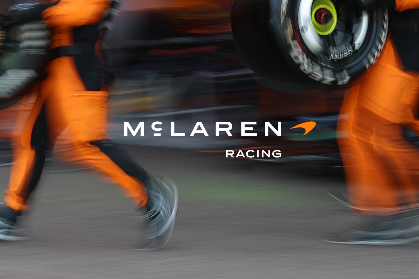 Pit alanında McLaren Racing yazısı ve turuncu tulumlu ekip