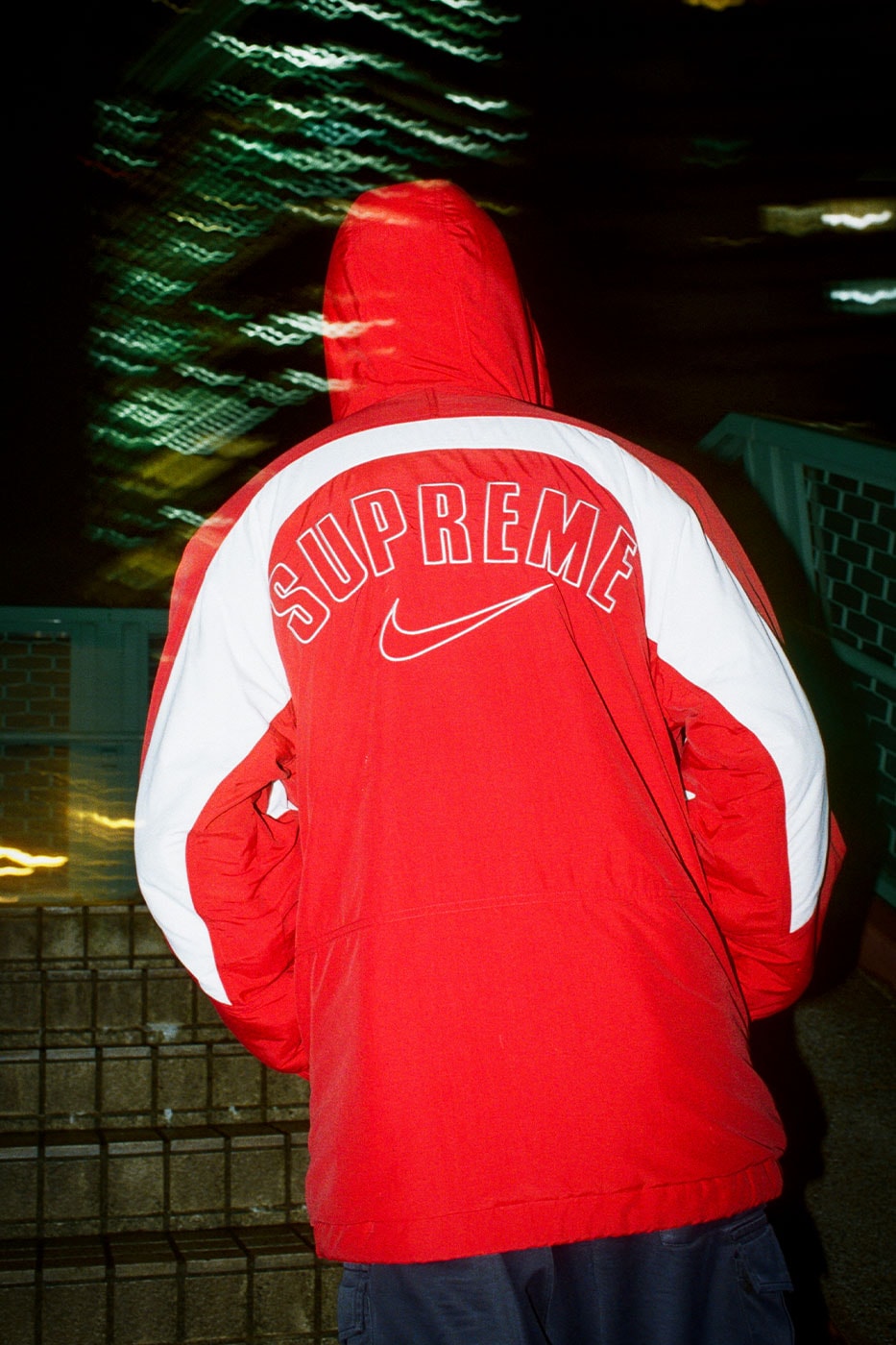 Kırmızı parkanın sırtındaki Supreme yazısı ve Swoosh