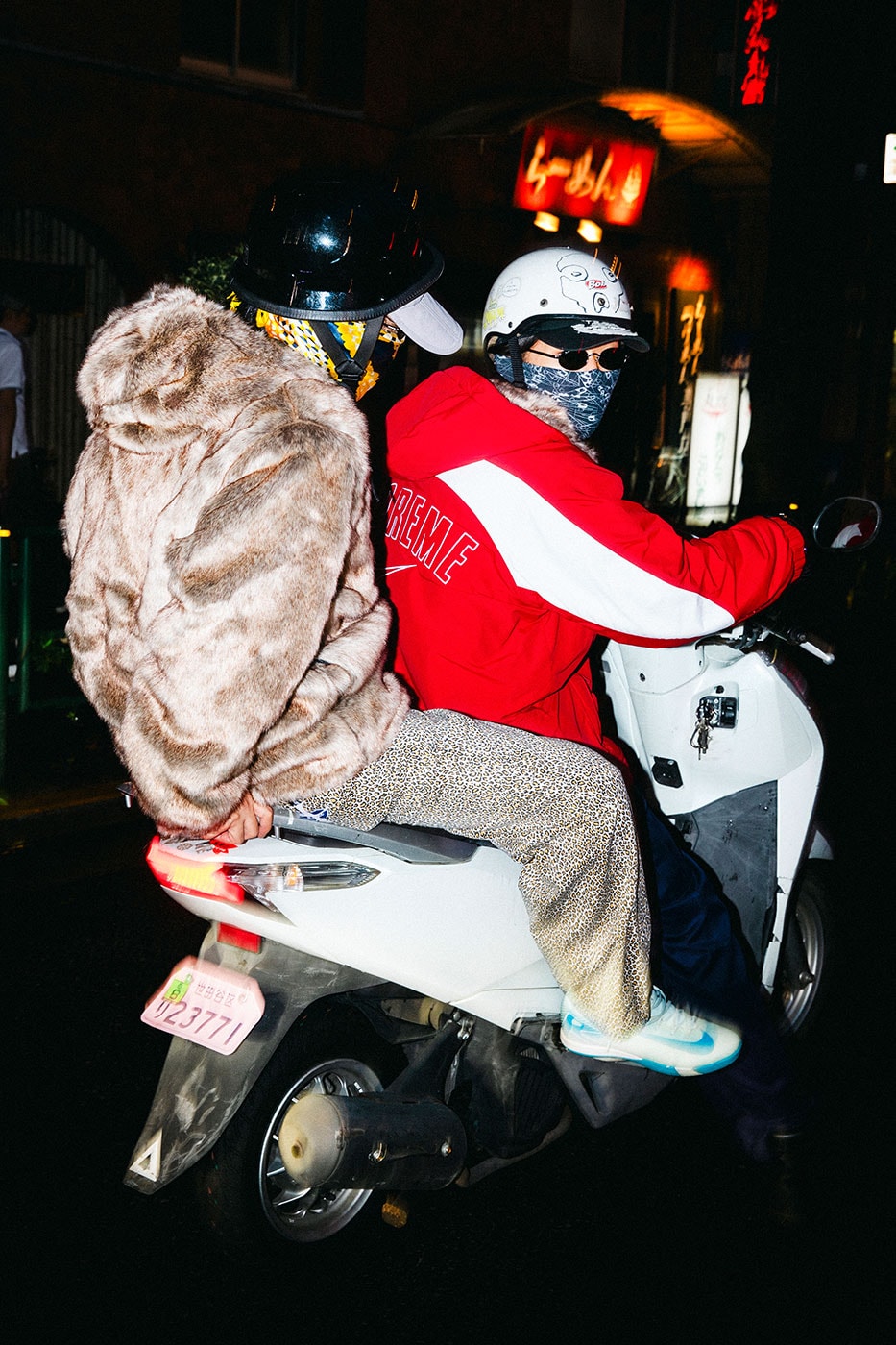 Motosiklette kürk ve kırmızı parka giyen iki kişi