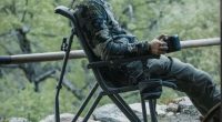 YETI Trailhead Field Chair ormanda, elinde termos bardağı olan bir kampçıyla