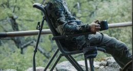 YETI Trailhead Field Chair ormanda, elinde termos bardağı olan bir kampçıyla