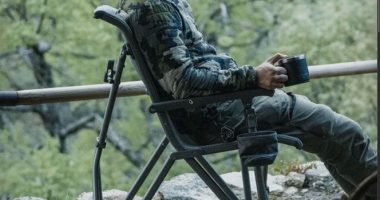 YETI Trailhead Field Chair ormanda, elinde termos bardağı olan bir kampçıyla
