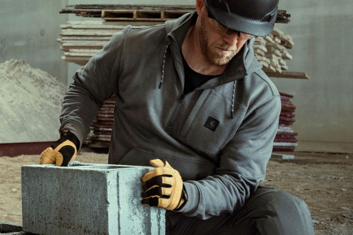 Gri sweatshirt giyen işçi beton blok taşıyor