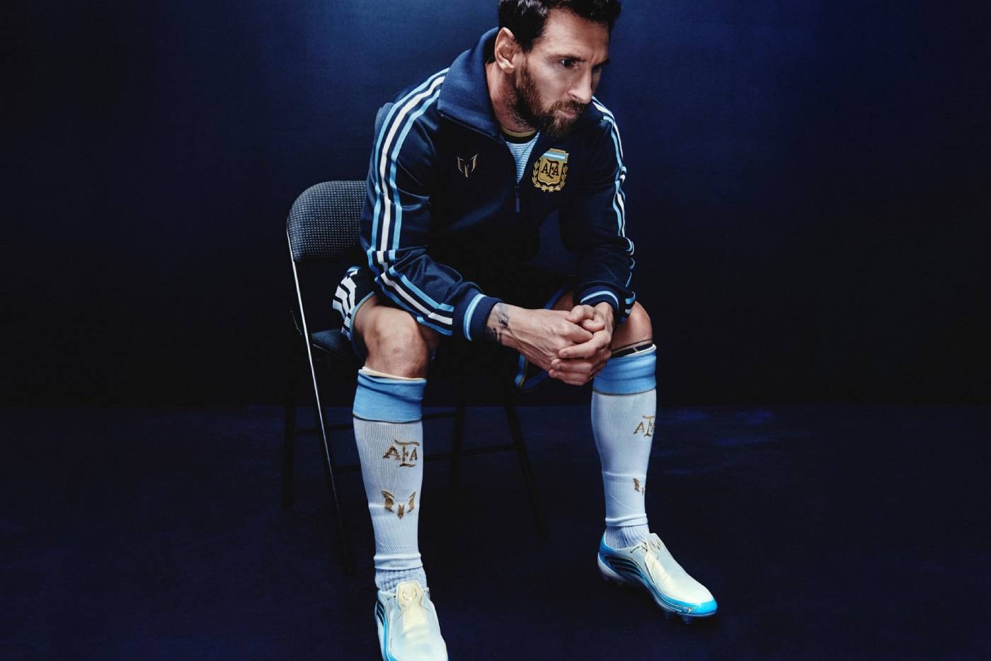 Sandalyede oturan, lacivert ceketli ve gök mavisi çoraplı Messi