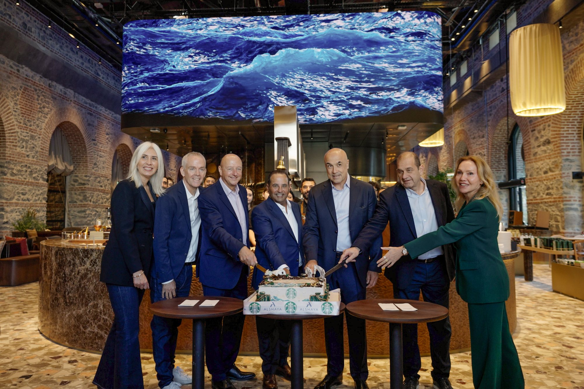Dalga ekranının altında Starbucks ve Alshaya logolu açılış pastasını kesen yöneticiler