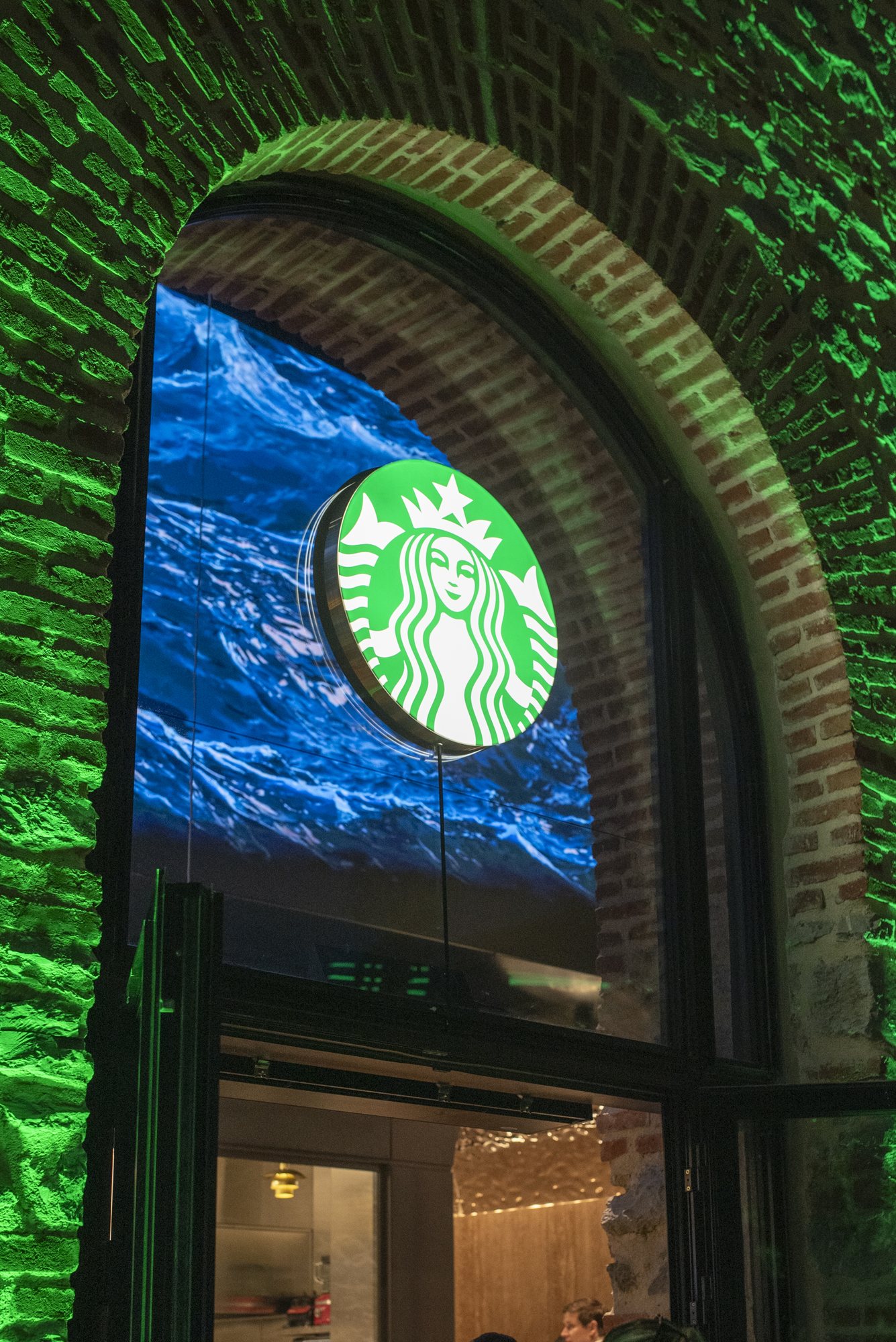 Yeşil ışıkla aydınlatılan tuğla kemerli girişte Starbucks logosu