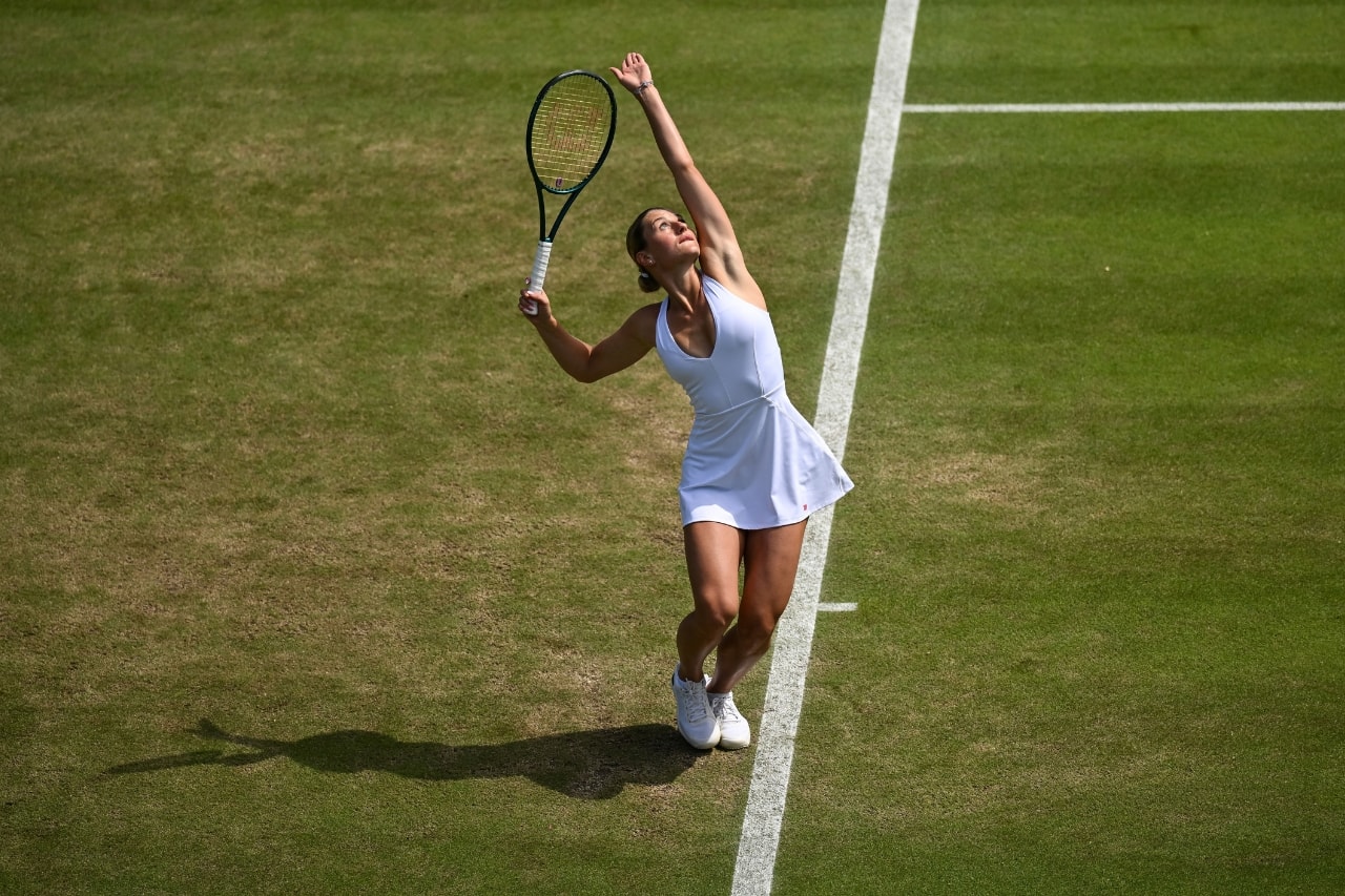 Wimbledon çim kortunda beyaz Wilson elbisesiyle servis atan tenisçi